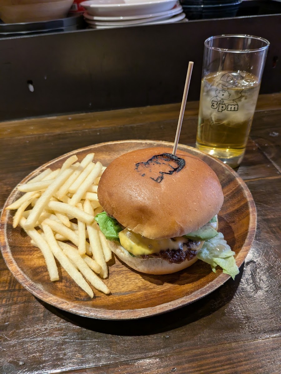 木の皿にのせたバーガーとフライドポテト。奥の木のカウンターに、キャップをかぶった絵の入ったグラスが一杯。